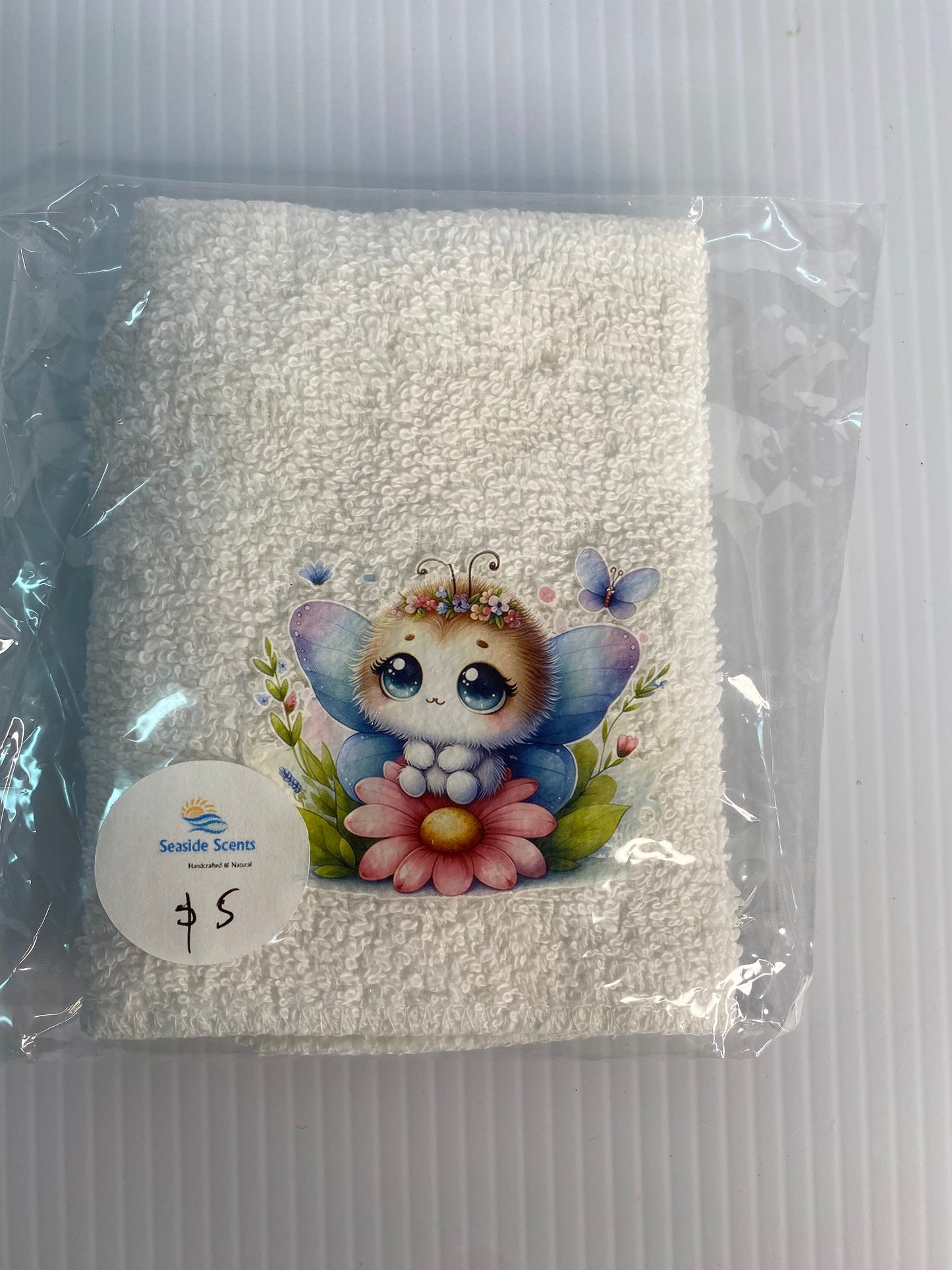 Baby Face Washer Furry Winged Baby sitting beside a pink flower on a White Washer